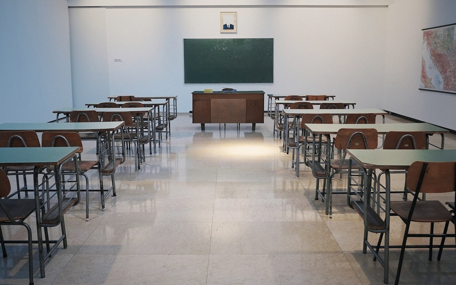 Empty classroom with rows of desks, a chalkboard, and a wall map
